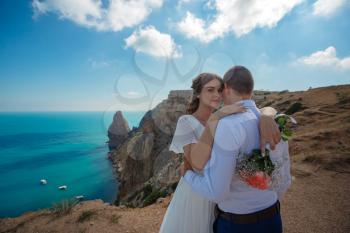 Beautiful smiling young bride and groom walking on the beach, kissing and having fun, wedding ceremony near the rocks and sea. Wedding ceremony on coast of Cyprus