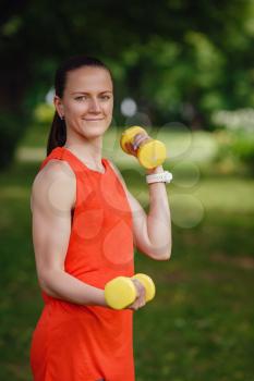 Sporty young woman with dumbbells outdoors. Doing fit activity and training,outside on green grass at park. Fitness, sport and healthy lifestyle