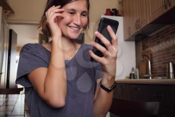 Happy woman using mobile phone for video call friends and parents, smiling girl sitting at home kitchen fun greeting online by computer webcam making videocall.