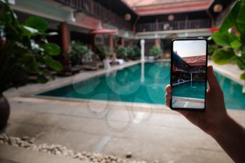 hand holding phone on background of the pool in hotel. photo camera on the screen. close up hand hold smartphone take a picture of summer vacation.