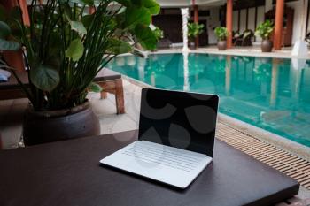 White laptop on the background of the swiming pool. Conceptual workspace. Freelancer, travel and vacation concepts.