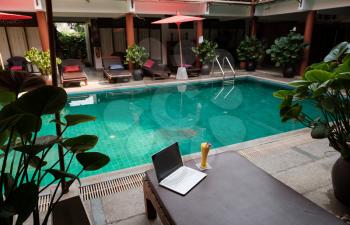 A white laptop, smartphone and mango smoothie on a sunbed against swiming pool background. A start of new day. Freelance business concept. Flexible remote working, travelling, advert and copy space