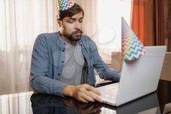 young man sitting at the table and talking by video call to friends. celebrating birthday online in quarantine time.