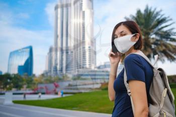Portrait of beautiful woman wearing a mask for prevent virus walking in Dubai with skyscrapers in the background. Enjoying travel in United Arabian Emirates.