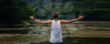 The young male hipster looking at the beautiful view at the lake. Beautiful freedom moment and peaceful atmosphere in nature. Back view.