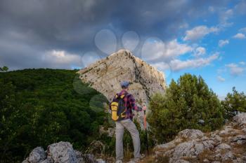 Young man standing on top of cliff in summer mountains at sunset and enjoying view of nature.