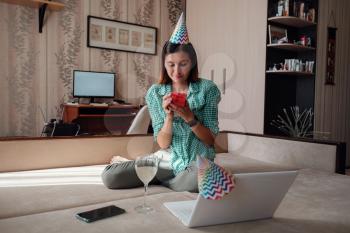 woman celebrating birthday online in quarantine time through video call virtual party. Coronavirus outbreak 2020. Woman opening a gift and have positive emotions.