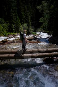 Hiker man hiking crossing river walking in balance on fallen tree trunk in landscape nature forest. Happy male hiker trekking outdoors in Dombai, Karachayevo-Cherkessia, Russia