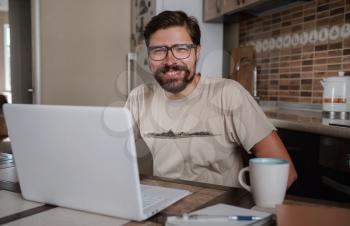 Satisfied with work done. Happy young man working on laptop while sitting at his working place in home office. Happy employee feeling no stress, relaxing, watching funny video after successful working