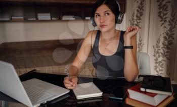 Young asian female student in headphones using laptop, writes notes . Cozy office workplace, remote work, E learning concept.