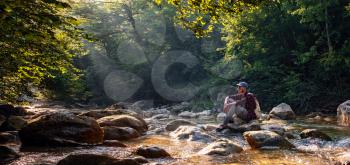 Happy male hiker trekking outdoors in forest near river. idea and concept of adventure, discovery and travel