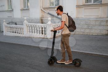 fun driving electric scooter through the city. A hipster man enjoys a walk through the city during the summer sunset. The idea and concept of ecology, style and fun moving around the city