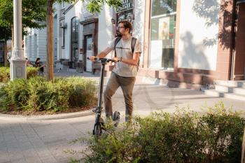 fun driving electric scooter through the city. A hipster man enjoys a walk through the city during the summer sunset. The idea and concept of ecology, style and fun moving around the city