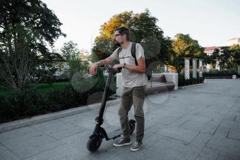 Attractive man riding a kick scooter at cityscape background. fun driving electric scooter through the city.