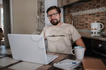 Satisfied with work done. Happy young man working on laptop while sitting at his working place in home office. Happy employee feeling no stress, relaxing, watching funny video after successful working