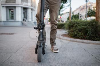 Close up of man riding black electric kick scooter at cityscape at sunset. Electric urban transportation concept image