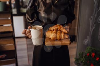 Close up female hand serving hot latte art coffee in white cup and croissant on wooden plate in coffee shop. Cafe drinking menu hot coffee at restaurant. Breakfast menu in the morning time.