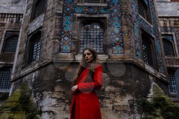 tourist woman visit ancient Istanbul Topkapi palace. Beautiful young woman in a red coat looks at the walls of the palace from the side of the park, Istanbul