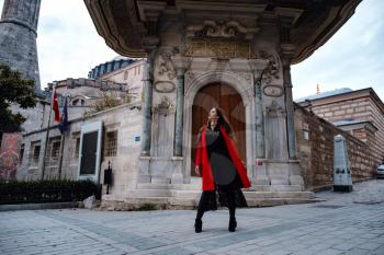 Woman enjoy walk near Hagia Sophia Cathedral, famous islamic Landmark mosque, Travel to Istanbul, Turkey. Latin American woman or Turkish woman in a red stylish coat