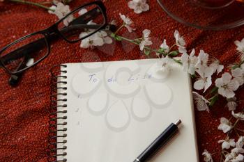 Spring flat lay top view home office workspace - notebook with tea cup and cherry blossom branches on a red desk background