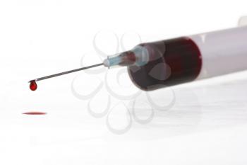 Macro view of drop of blood from syringe over white background. Blood chemistry. Blood test for viruses.