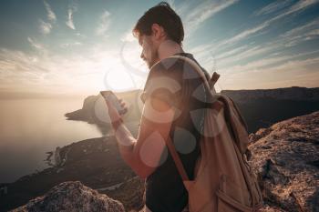 Man backpacker using smartphone relaxing on mountain top traveling alone. lifestyle active vacations modern technology millennials concept. Marvelous daybreak. mock up text.