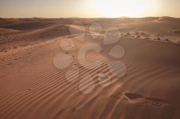 Sunset over the sand dunes with footprints in the desert. The ghost town of Al-Madam is about 60 km from Dubai City. united arab emirates. The concept of global warming