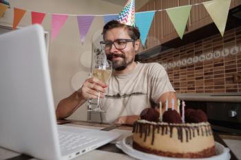 Man celebrating birthday online in quarantine time. Guy celebrating his birthday through video call virtual party with friends. Coronavirus outbreak 2020.