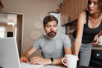 Young couple using laptop and smartphone in the kitchen, smiling man working online at home, family morning lifestyle with gadgets or devices addiction concept. readings news