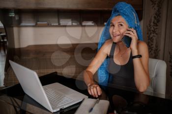 Shot of pretty young woman using her mobile phone while working with laptop sitting at home. Working from home in quarantine lockdown. Social distancing Self Isolation