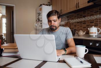 young man freelancer using laptop studying online or working from home, happy casual millennial guy typing on pc notebook surfing internet looking at screen enjoying distant job sit at table
