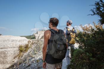 Two Men walking on rocky slope carrying Backpacks using trekking Sticks. Mountains valley View beside of People. summer travel to nature