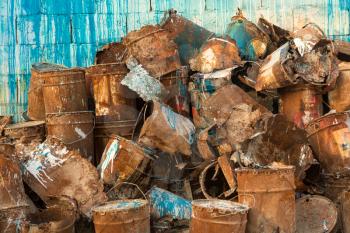 Stack or pile of old rusty metal paint cans with blue and white paint running from the stack