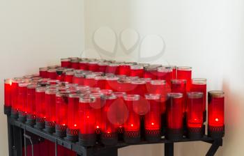 Simple rows of red lit votive candles in plain white painted catholic church interior