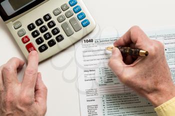 Male caucasian hand holding pen above USA tax form 1040 for year 2014  and calculator illustrating completion of tax forms for the IRS