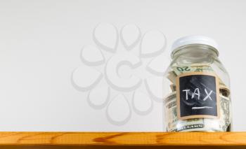 Single glass jar with chalk labels used for saving US dollar bills and notes for tax and taxes