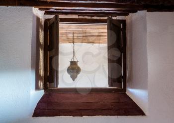 Wooden shutters closing window in thick stone wall of house with small ornate lamp hanging from beams outside