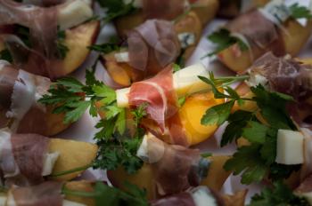 White plate full of home made appetizers with peach slice and gorgonzola cheese wrapped by strip of prosciutto ham