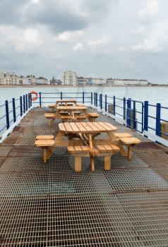View across and empty deserted tables and benches at the end of the pier in Eastbourne looking towards the promenade