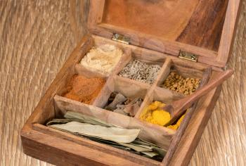 Collection of different oriental indian curry spices in wooden box with turmeric in wood spoon on table top