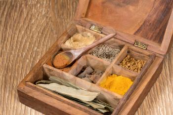 Collection of different oriental indian curry spices in wooden box with ginger in wood spoon on table top