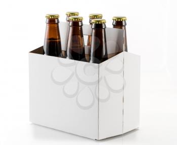 Six beer bottles in cardboard container with gold caps with corner of carrier facing camera