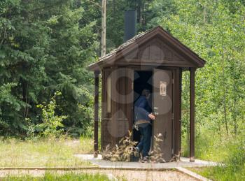 Wooden restroom or toilet in remote forest with woman entering through wooden door