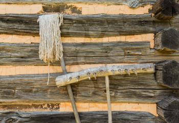 Old hand made farming tools of wooden rake and string mop leaning against log cabin walls