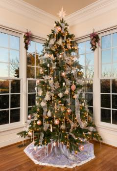 Ornately decorated and lit Christmas tree in the corner of a modern family home with trees lit by setting sun
