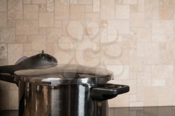 Stainless steel pressure cooker letting off steam on a modern induction cooking hob with glass top