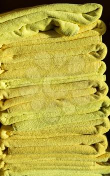 Tall stack of yellow bath or beach towels with the sun shining on the pile from the side giving a warm glow to the toweling