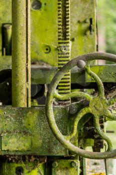 Green lichen covered farm machinery abandoned in forest with turning handle and cogs and gears
