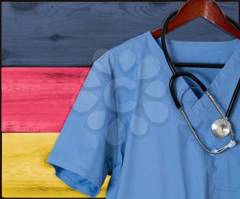 Blue doctor scrubs shirt and stethoscope hang empty in front of German flag. Illustration of medical staff coming from other countries to staff health systems