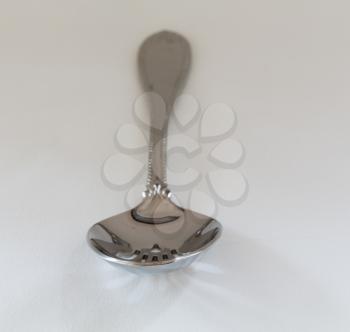 Decorated slotted serving or dessert spoon for draining wet vegetables in front view on fine white tablecloth with pattern just visible